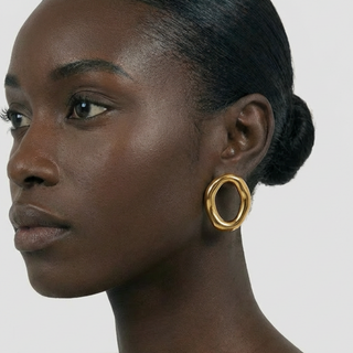 Woman wearing a gold hoop earring on a plain background
