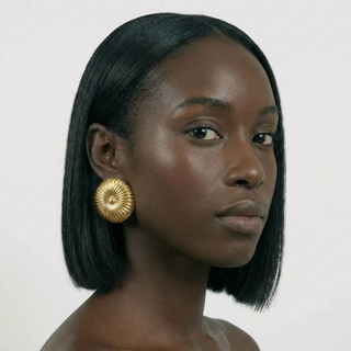 Woman wearing gold earrings with a plain background