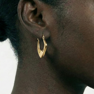 Gold hoop earring worn by a person with a neutral background