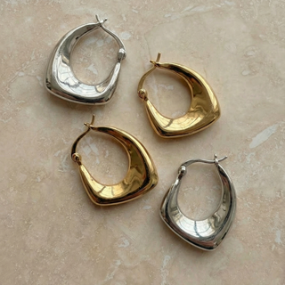 Four hoop earrings in gold and silver on a beige marble surface