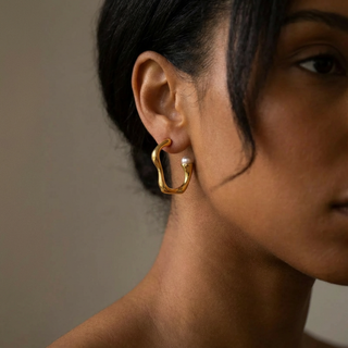Close-up of a person wearing a gold hoop earring with a pearl accent.