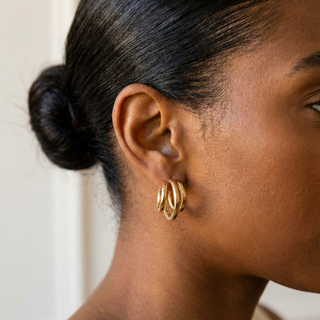 Close-up of a person wearing gold hoop earrings with a neutral background